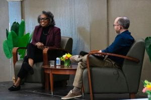 Robin Glover and Chris Lewis seated onstage, talking, while Robin is smiling.